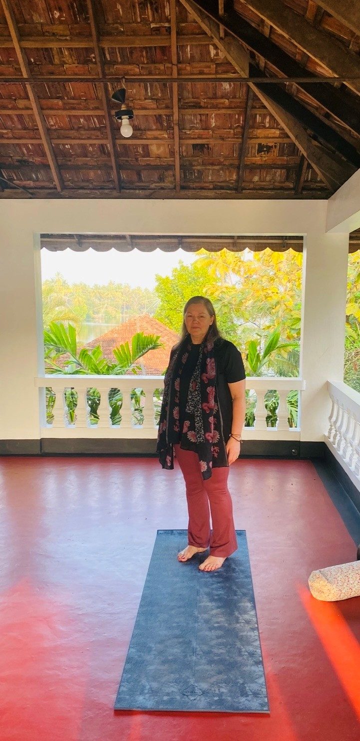 Sam standing on a yoga mat in an open-air shala in India